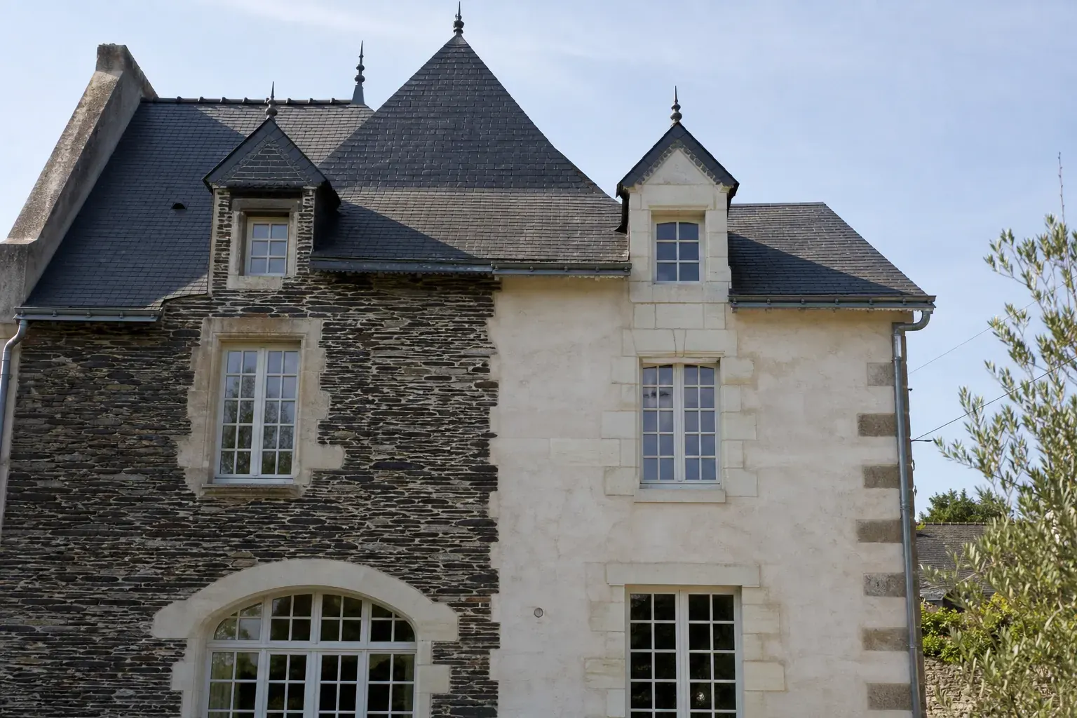 Façade angevine juxtaposant un mur en pierre de schiste sombre et un mur en pierre de tuffeau blanc, toiture d’ardoise