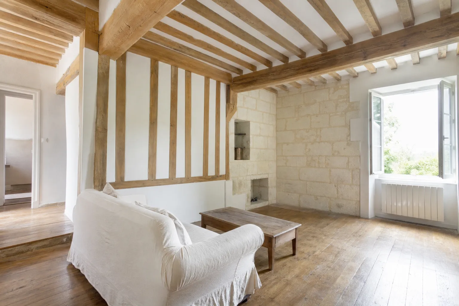 Séjour d’une maison ancienne rénovée avec poutres apparentes, mur en pierre de tuffeau et parquet ancien poncé